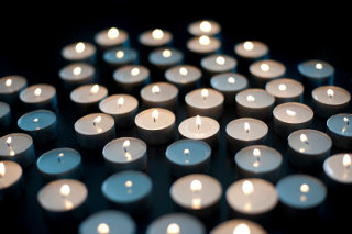 Array of small round burning candles against a dark background